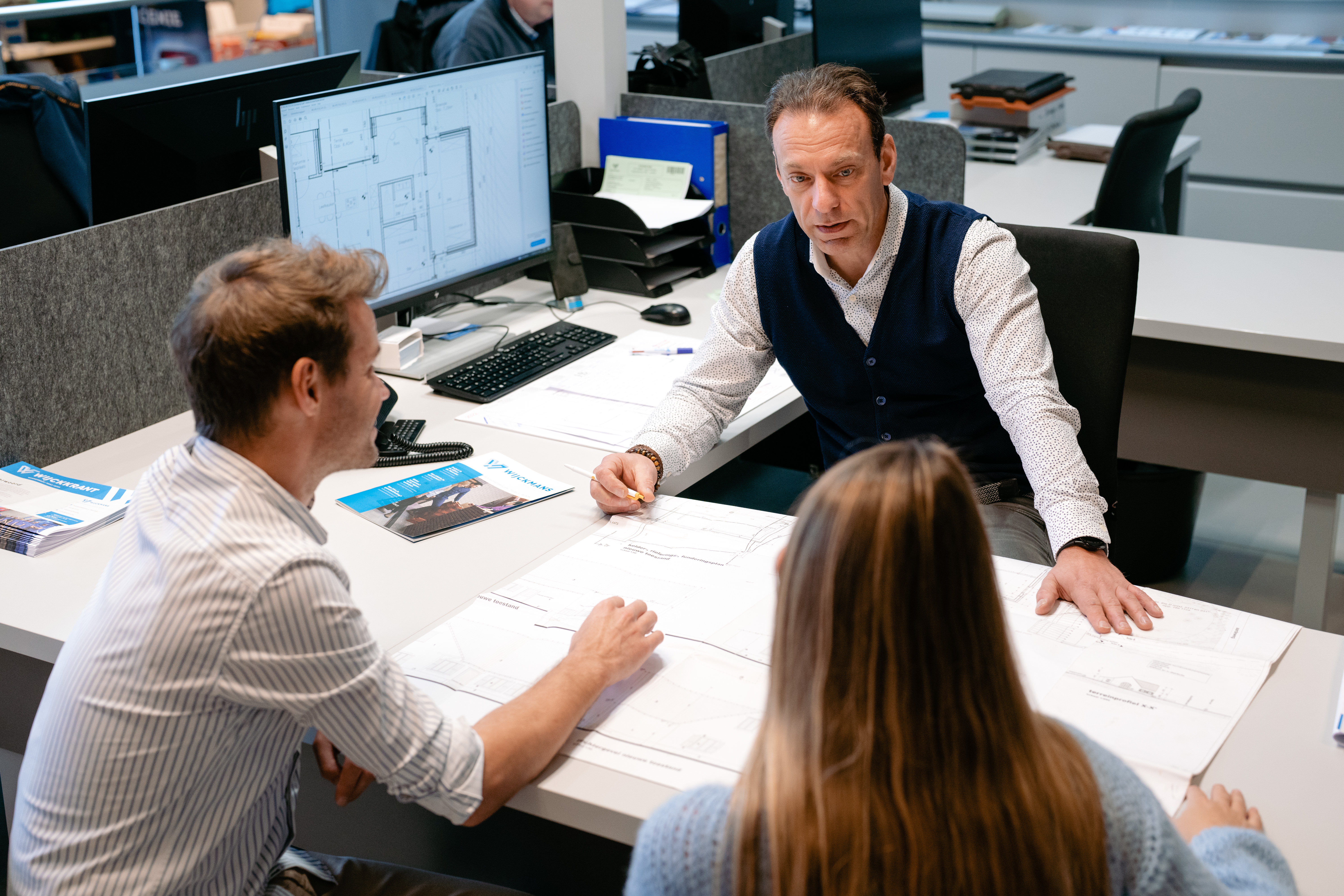 Een expert van Wijckmans zit aan tafel met klanten en bekijkt samen met hen werfplannen.